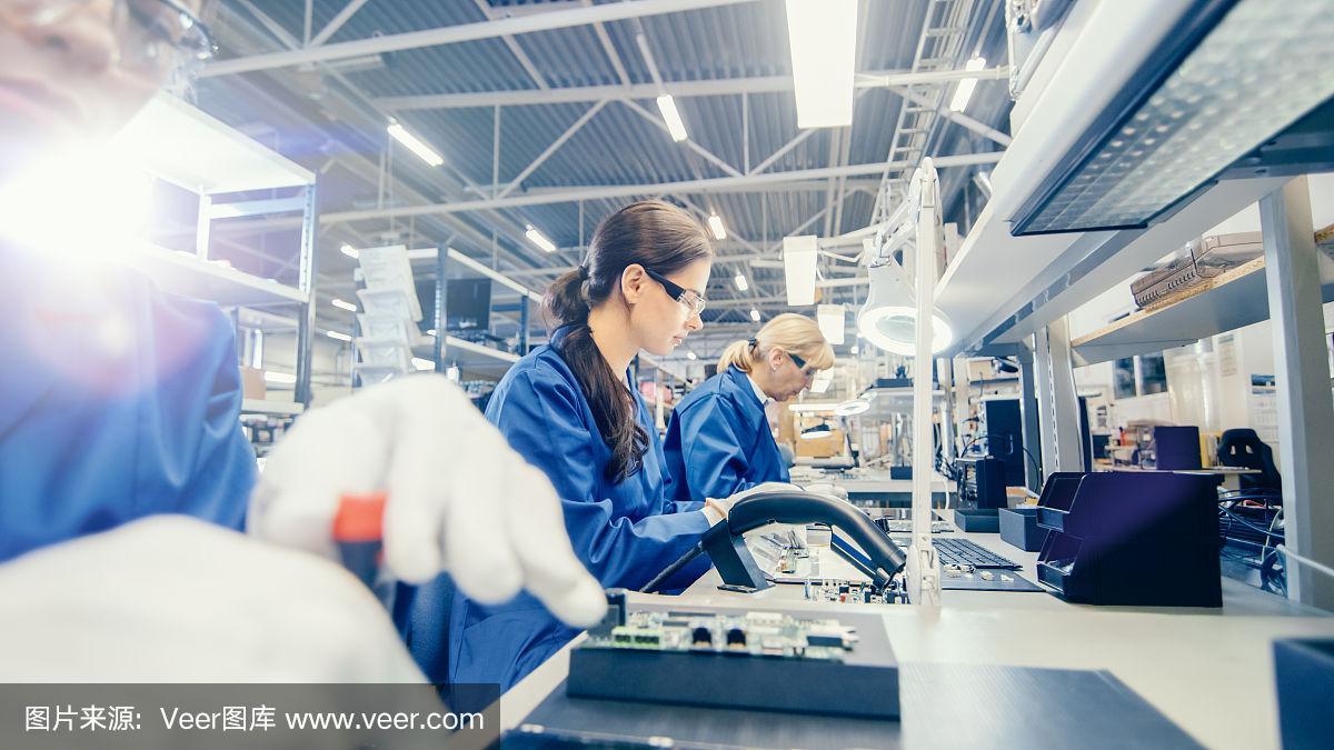女電子工廠的工人在藍色的工作外套和保護眼鏡組裝筆記本電腦的主板與